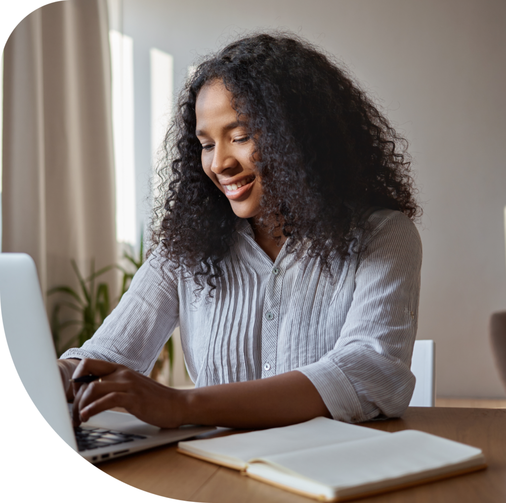 A person who is happy and working with her computer and a open notebook.